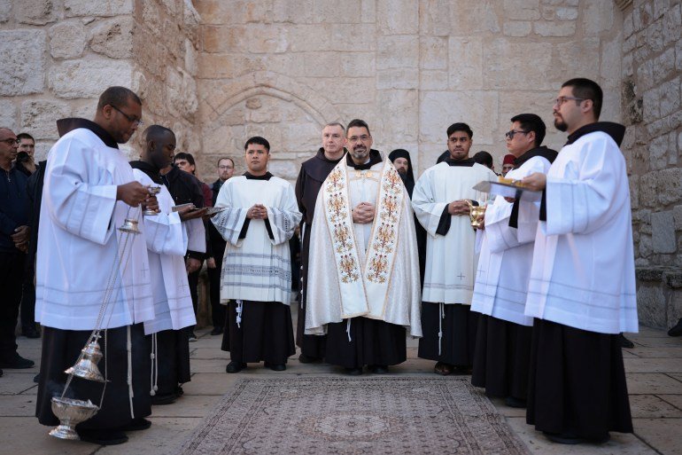 Clergymen and alter boys wait before Christmas service in the Manger Square outside the Church of the Nativity in Bethlehem