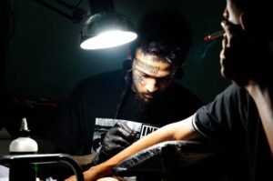 Ng La tattooing a fellow Myanmar national in exile, in the back of his 'punk bar' [Ali MC/Al Jazeera]