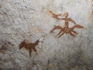 This image provided by Maxime Aubert shows cave drawings in Sulawesi, Indonesia of a human figure and a bird with a faded handprint in between them. (Maxime Aubert via AP)