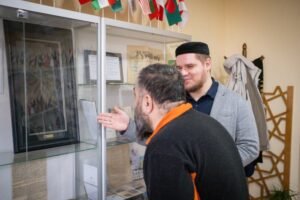 Zhumabekov motions to a small piece of the Kiswa, the black cloth that covers the Kaaba in Mecca, which has been framed and put in a display cabinet, Lviv, Ukraine, January 29 2026 [Nils Adler/Al Jazeera]