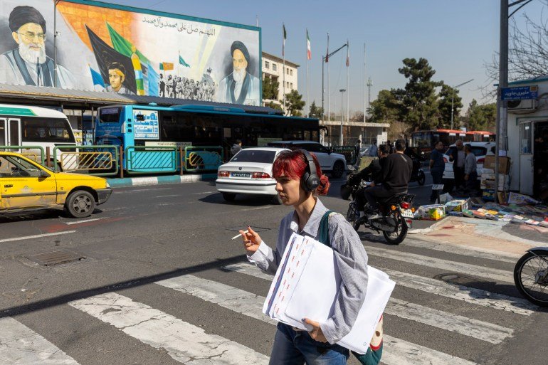 TEHRAN, IRAN - FEBRUARY 21: An Iranian woman walks across a main street in Tehran with the background of a large poster of Iran's supreme leaders, Ayatollah Ali Khamenei and Ayatollah Ruhollah Khomeini on February 21, 2026 in Tehran, Iran. In recent weeks, the United States has moved vast numbers of military vessels and aircraft to Europe and the Middle East, heightening speculation that it intended to strike Iran. (Photo by Majid Saeedi/Getty Images)