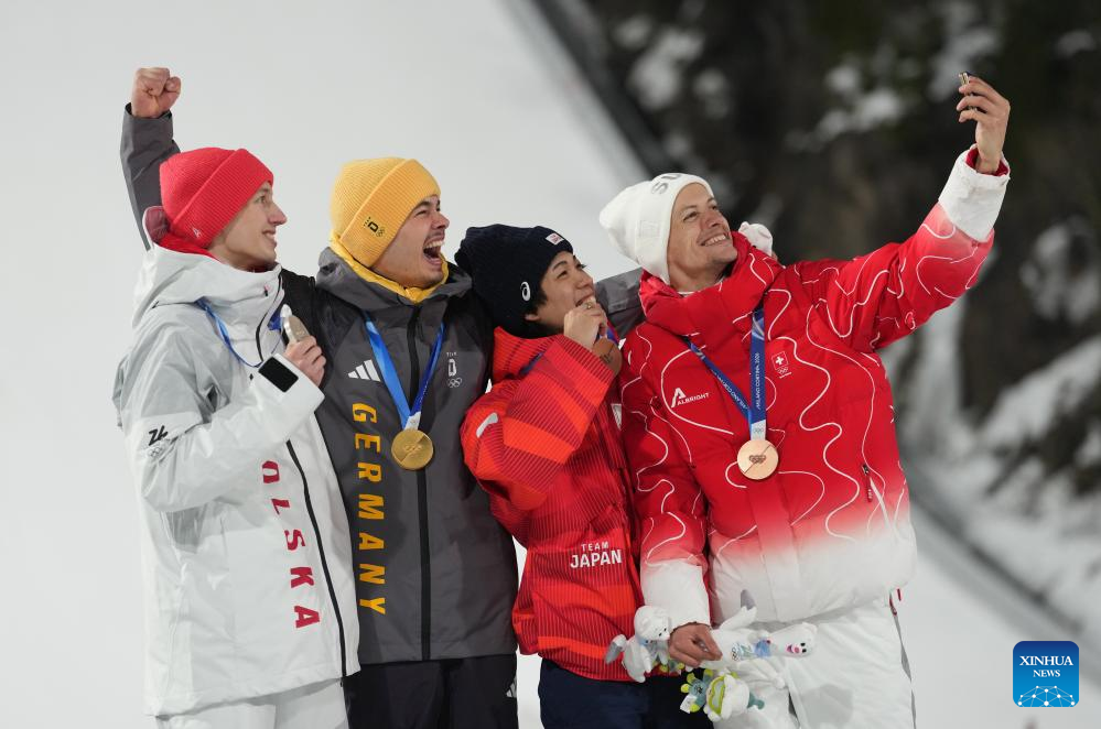 O medalhista de ouro Philipp Raimund, da Alemanha (2º L), o medalhista de prata Kacper Tomasiak, da Polônia (1º L), os medalhistas de bronze Nikaido Ren (2º R), do Japão, e Gregor Deschwanden, da Suíça, posam para selfies durante a cerimônia de premiação do Individual Masculino de Salto de Esqui em Normal Hill dos Jogos Olímpicos de Inverno de Milão-Cortina 2026, em Predazzo, Itália, em 9 de fevereiro de 2026. (Xinhua/Meng Yongmin)