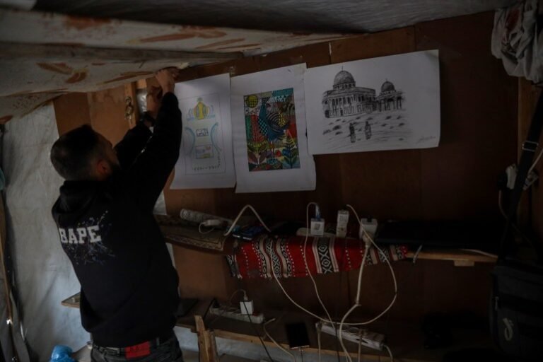 Abdulrahman hangs what remains of his artwork inside the charging point, which now serves as his source of income [Abdelhakim Abu Riash/ Al Jazeera]