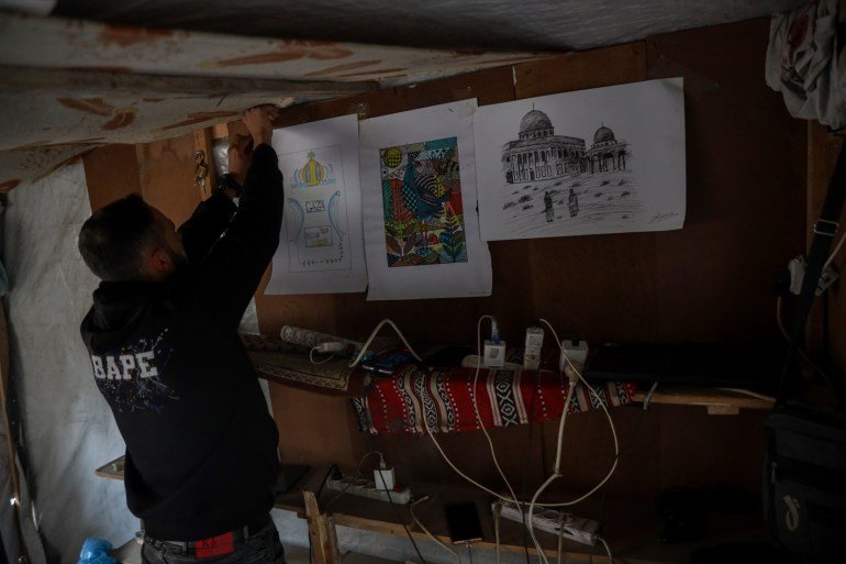 Abdulrahman hangs what remains of his artwork inside the charging point, which now serves as his source of income [Abdelhakim Abu Riash/ Al Jazeera]
