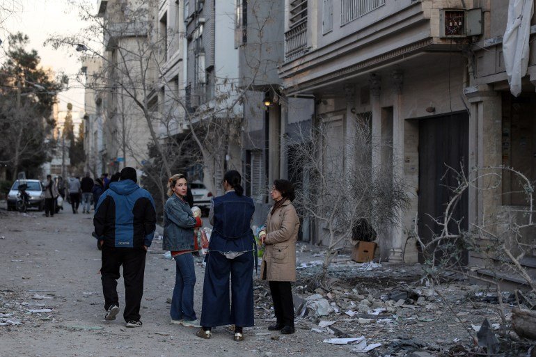 Residents stand on a street beside damaged residential buildings near Niloufar square in Tehran during the ongoing joint US-Israeli military campaign on Iran on March 2, 2026.