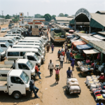 Busy outdoor market with people, white trucks, and a sign at a gas station saying no fuel available