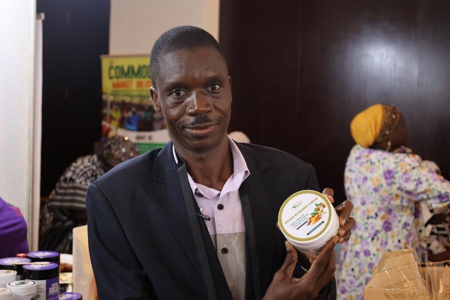 Daniel Kombat, CEO da Danikom Ghana Limited, produtora de manteiga de karité natural e sabonete preto africano, posa para fotos com produtos de manteiga de karité em um estande de exposição durante a conferência Shea 2026 em Accra, Gana, em 28 de abril de 2026. (Foto por Seth/Xinhua)